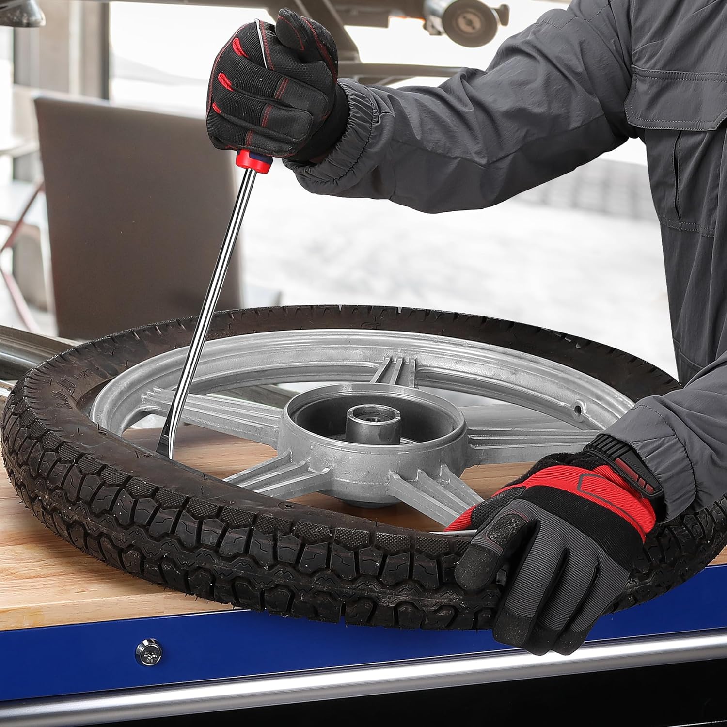 Tire lever prying a tire off a wheel rim with blue-and-red handle and gloves