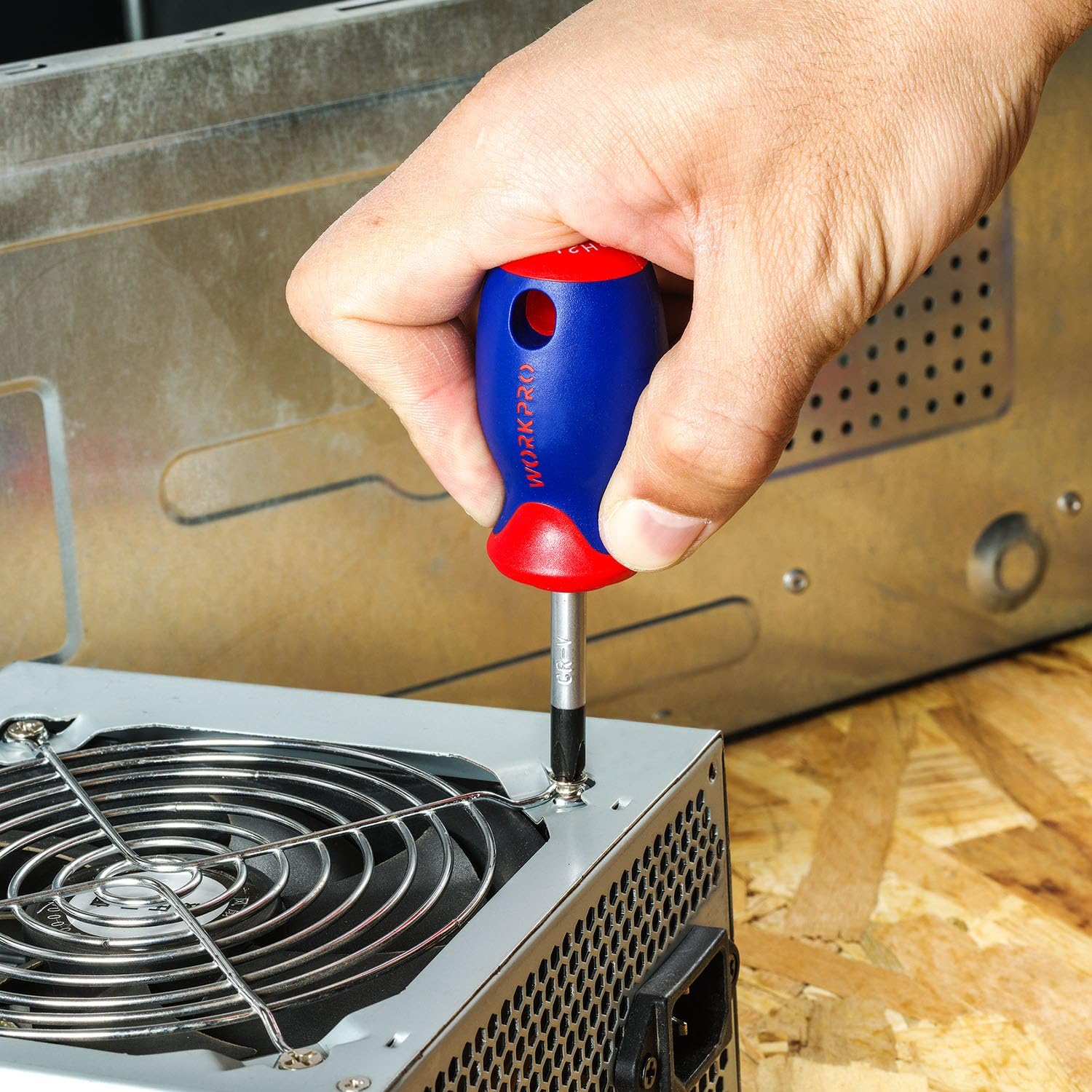 Hand using blue-and-red screwdriver on metal computer panel near vent