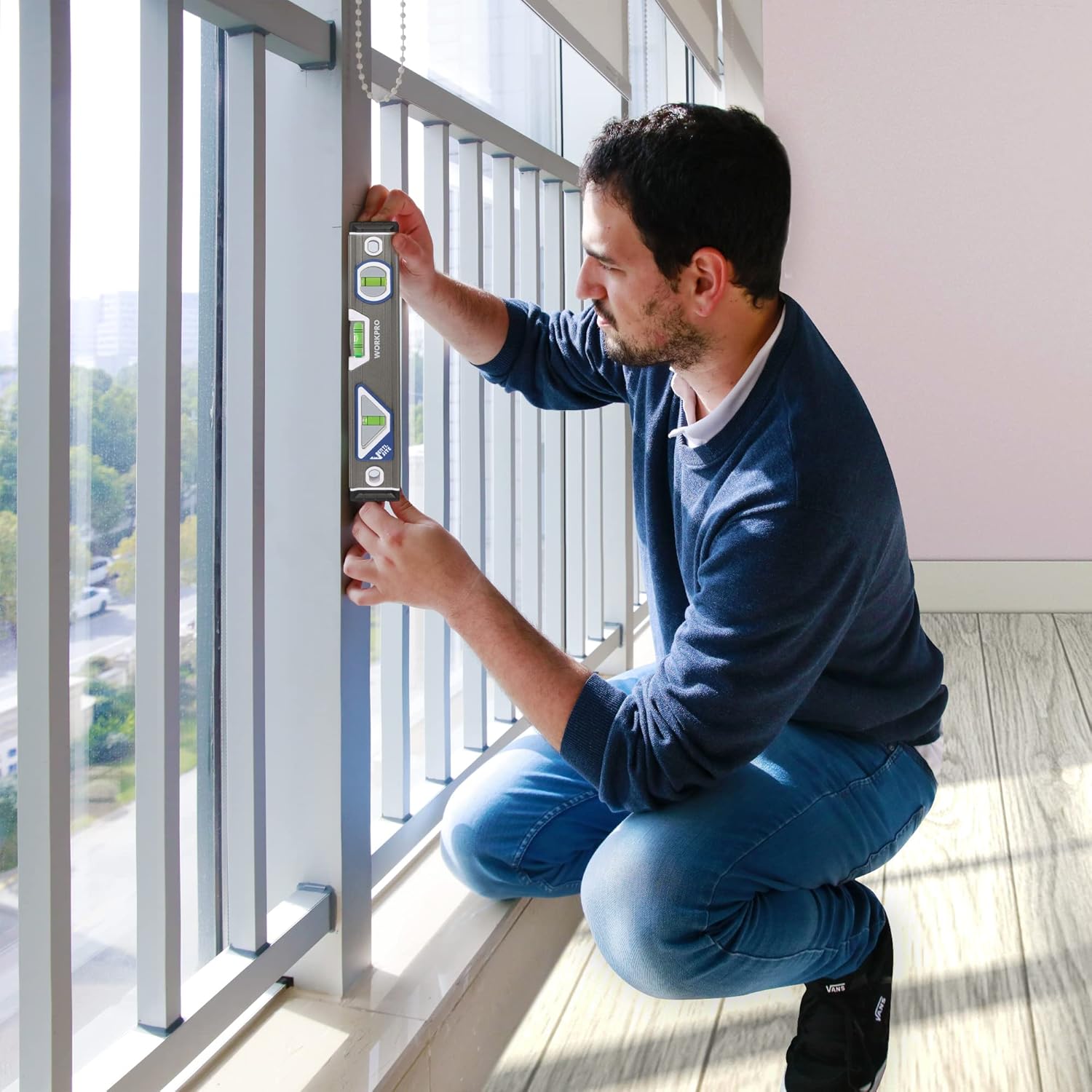 Person kneeling and using compact torpedo level to measure vertical alignment