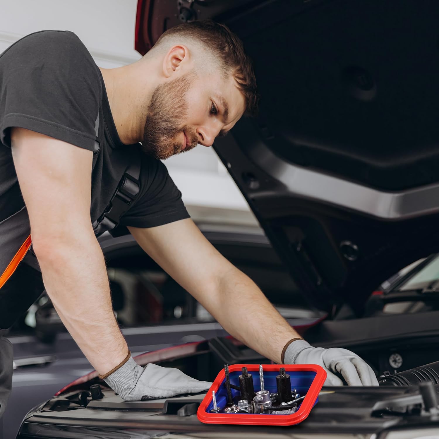 Red magnetic parts tray set holding screws on a vehicle engine bay