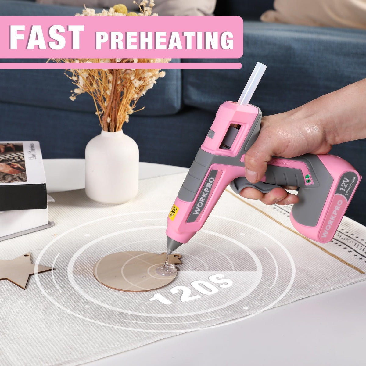 Hands using a pink 12V hot melt glue gun on a fabric surface with glue flow