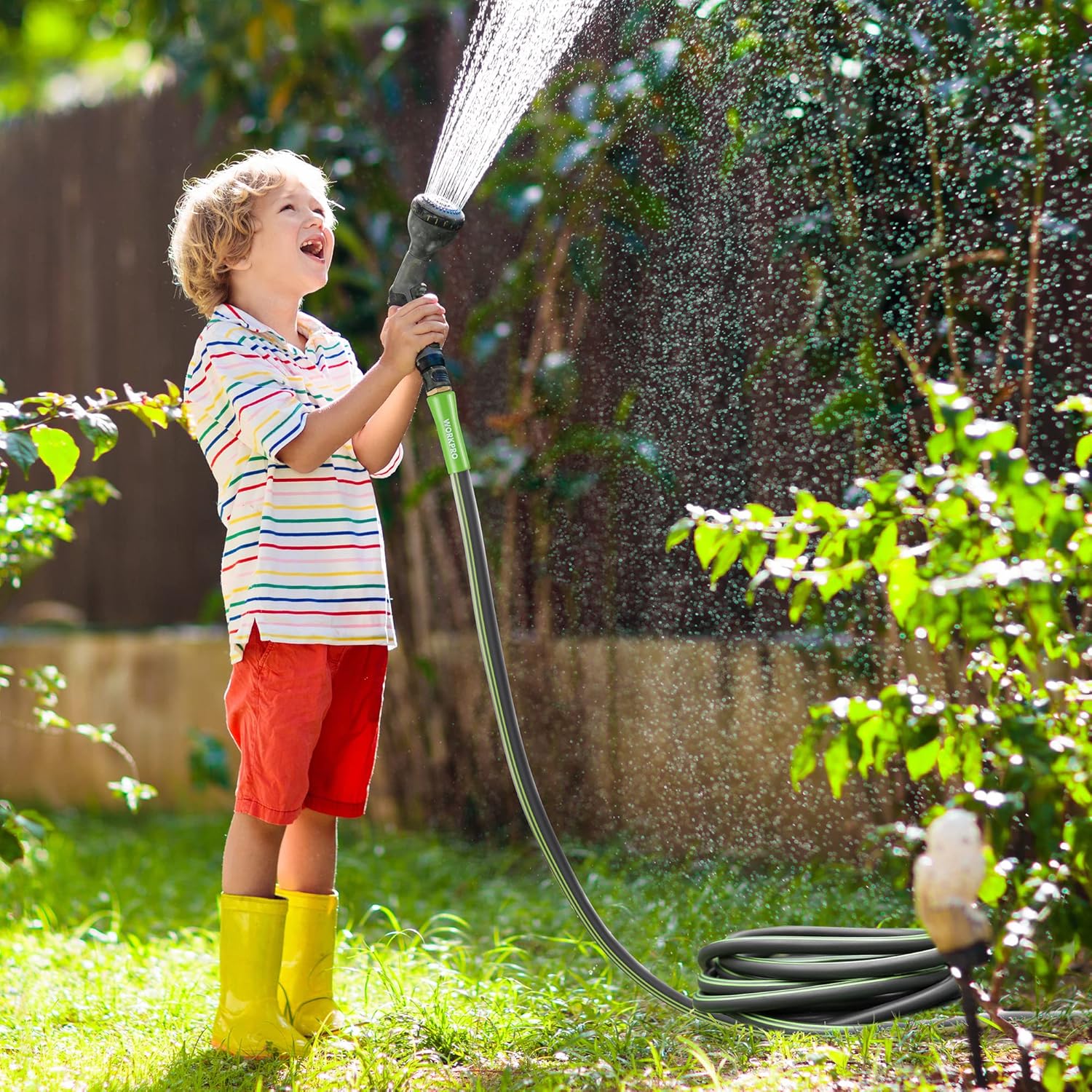Outdoor garden hose spraying water from green nozzle, flexible black tube