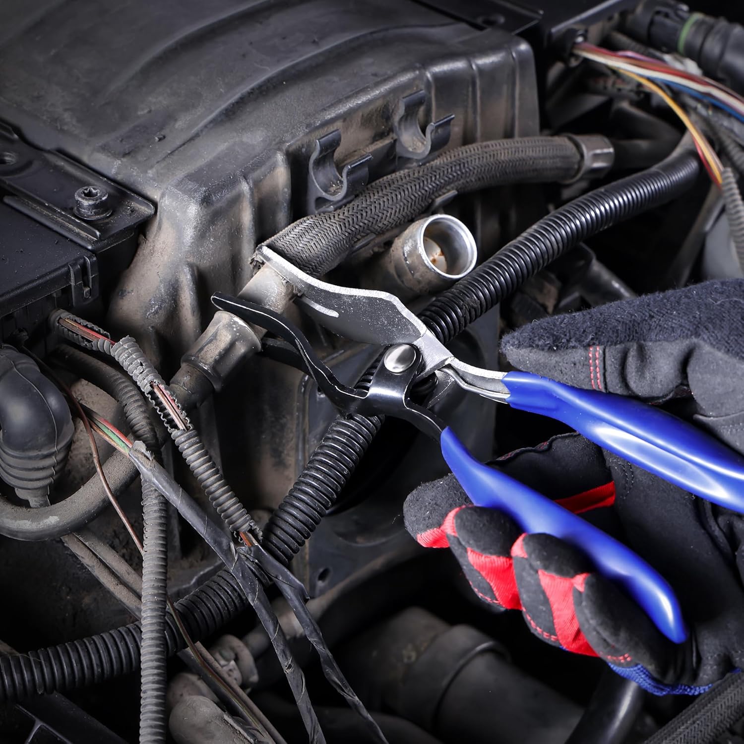 Blue hose removal pliers working on a vehicle hose clamp in tight engine space