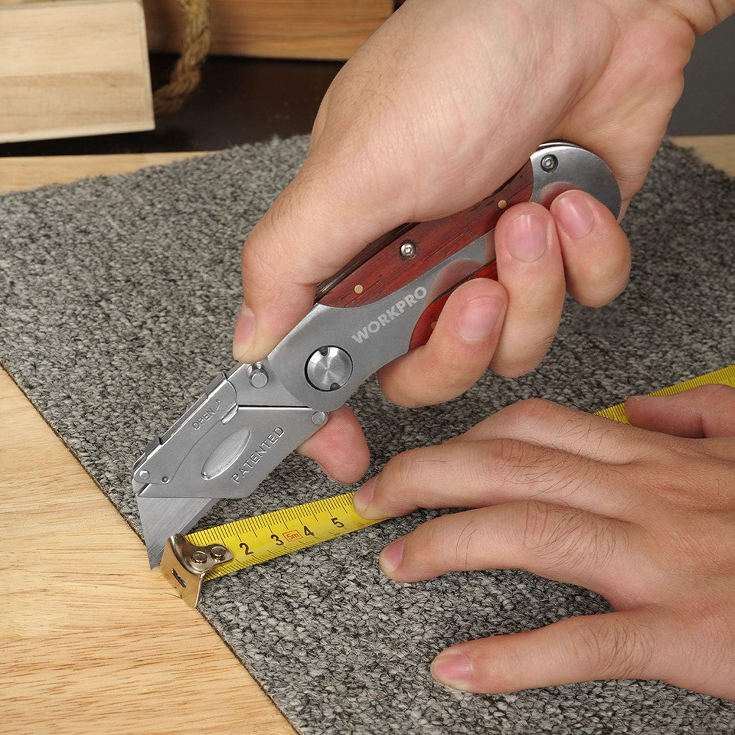 Folding utility knife in use near a measuring tape on wood and carpet