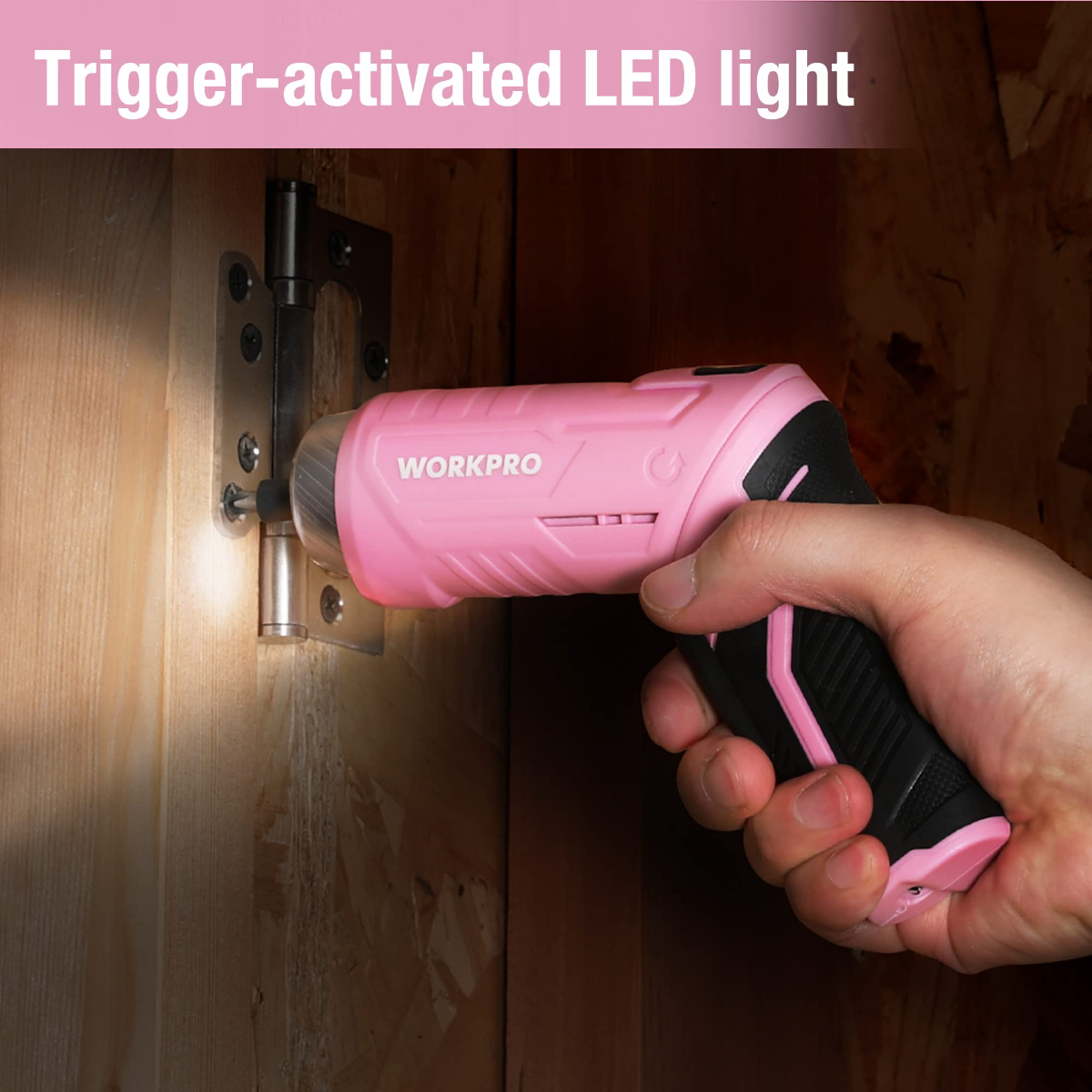 Pink WORKPRO cordless screwdriver triggering LED light while held near a wooden door hinge