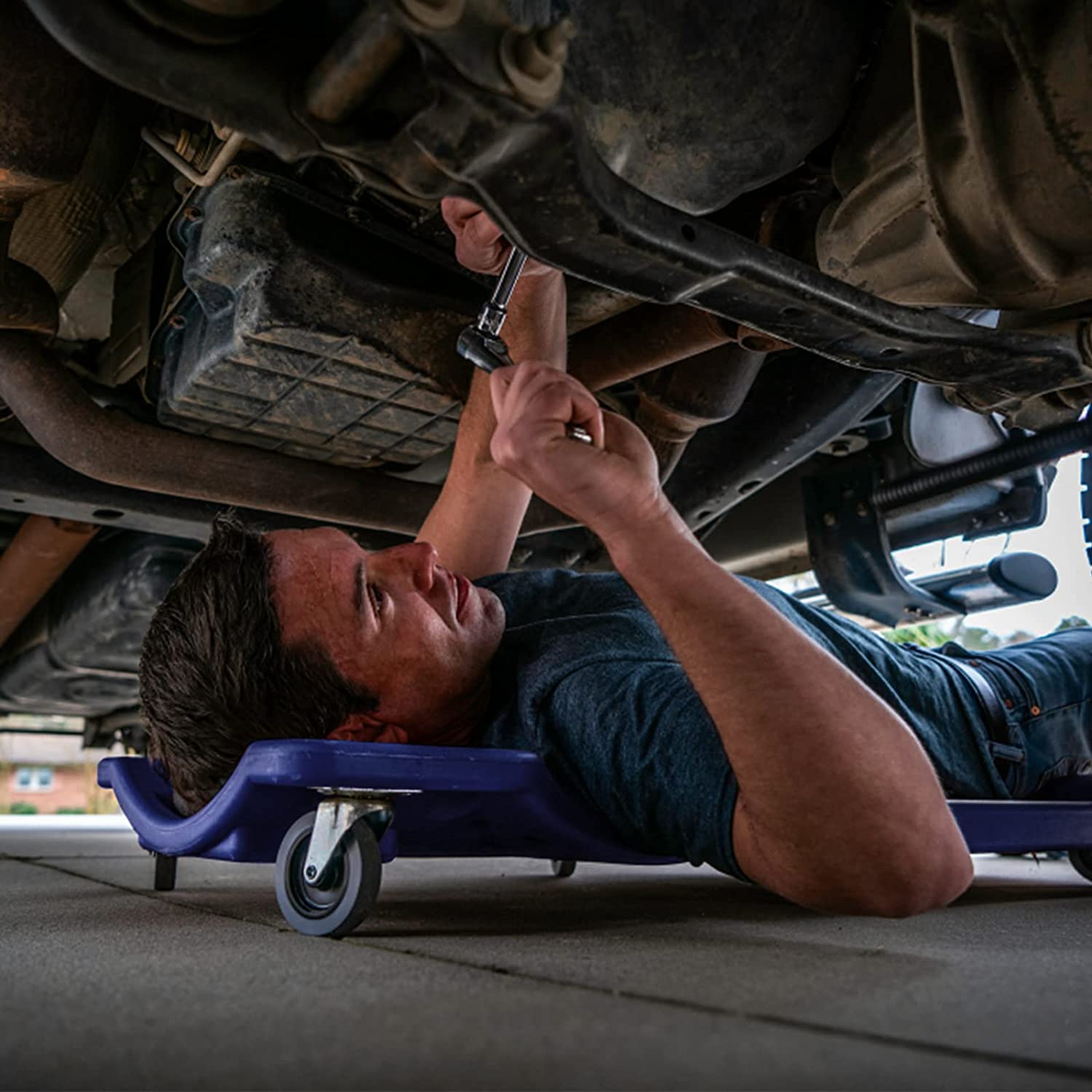 Blue mechanic creeper with padded headrest under a vehicle, with rolling casters