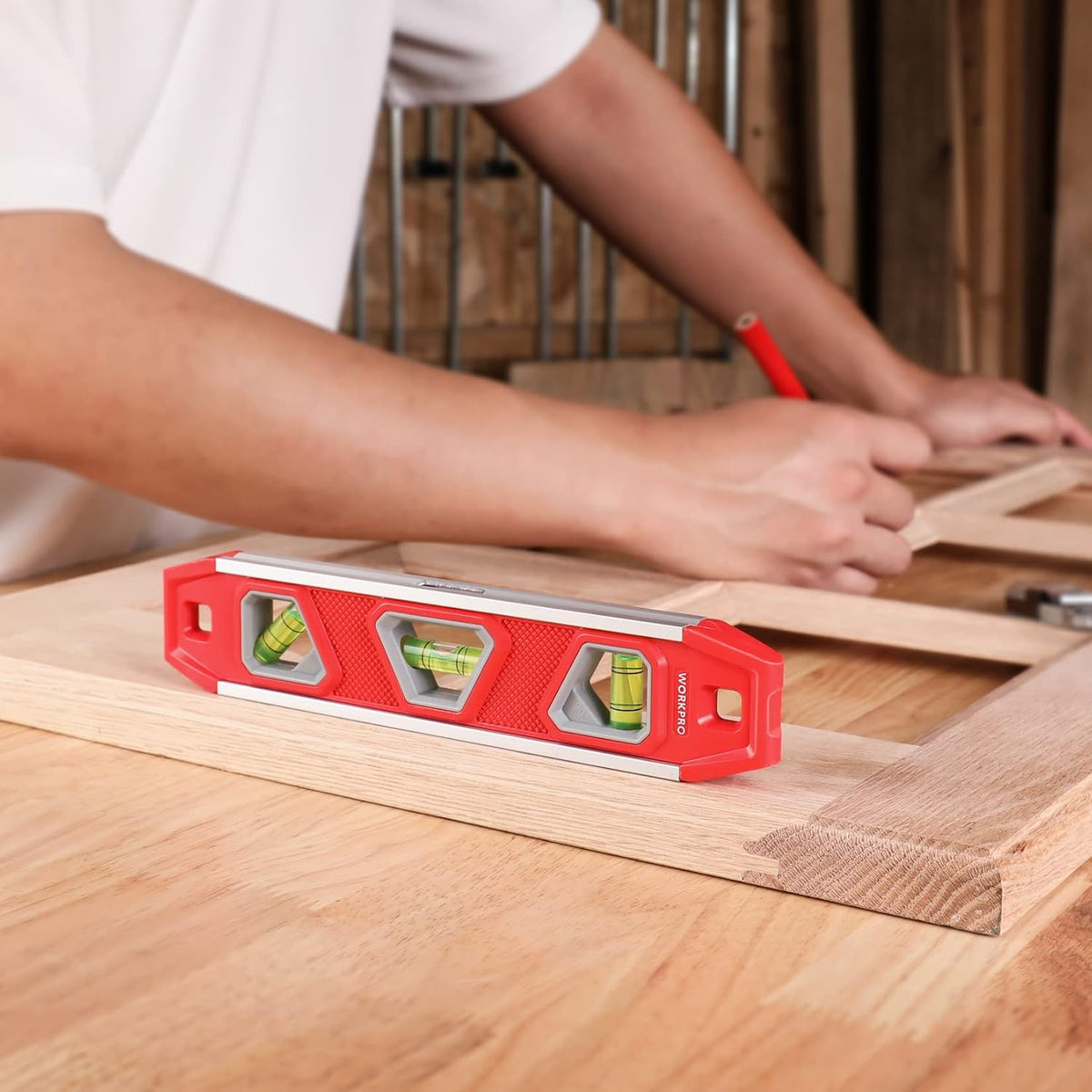 Red magnetic torpedo level placed on wooden board with three vials for leveling.