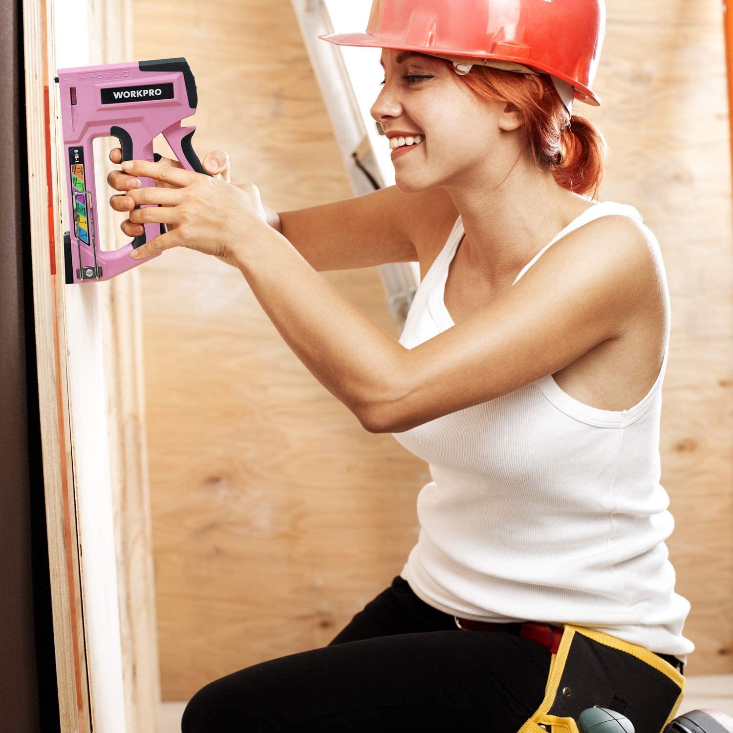 Pink manual brad stapler held to a wooden surface, ready to fasten