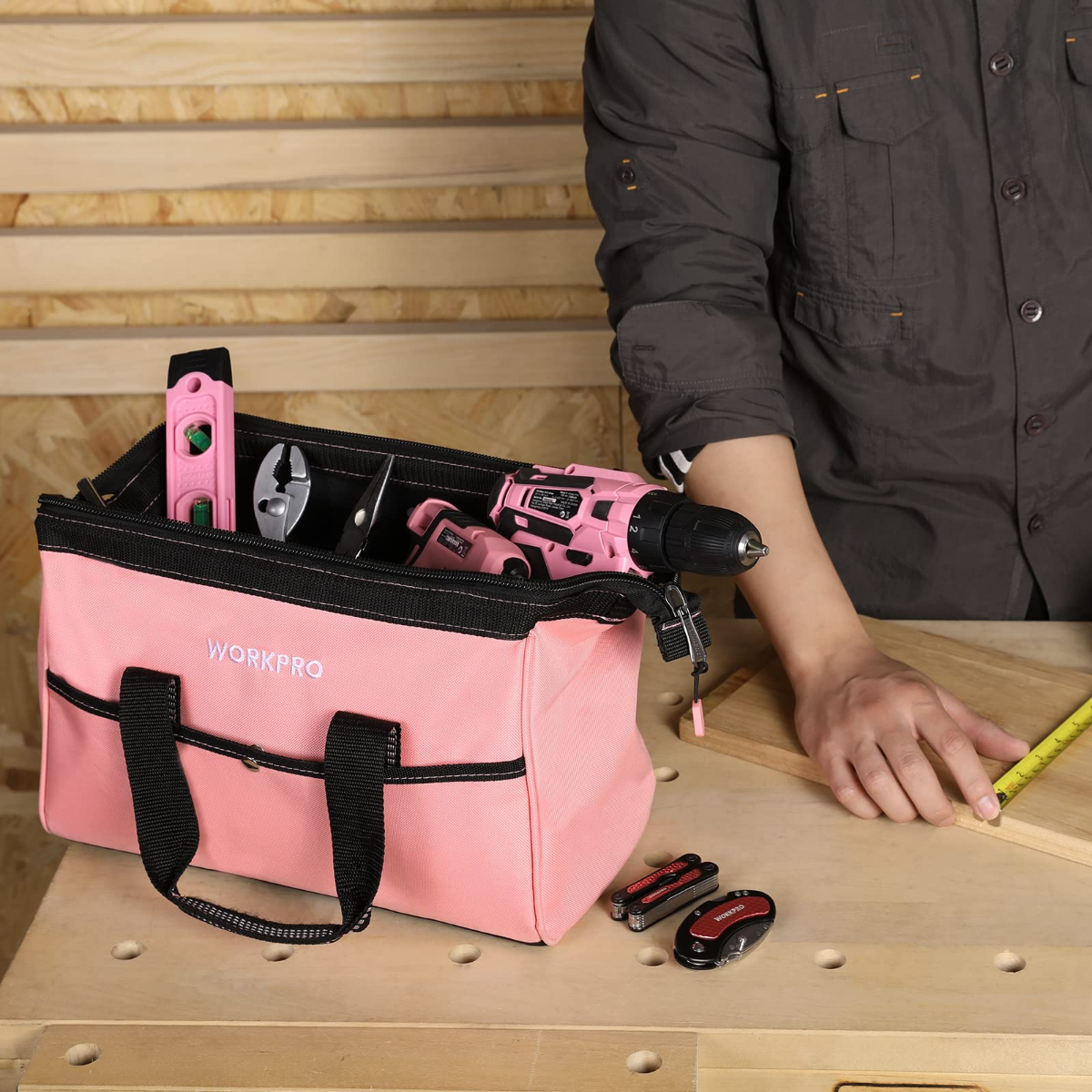 Pink tool bag with black trim and front pockets, set on a workbench with tools.