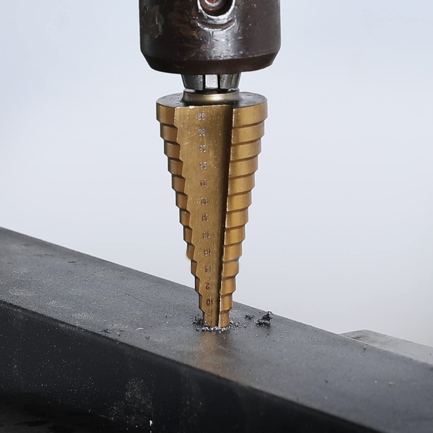 Titanium-coated step drill bit cutting into a metal sheet