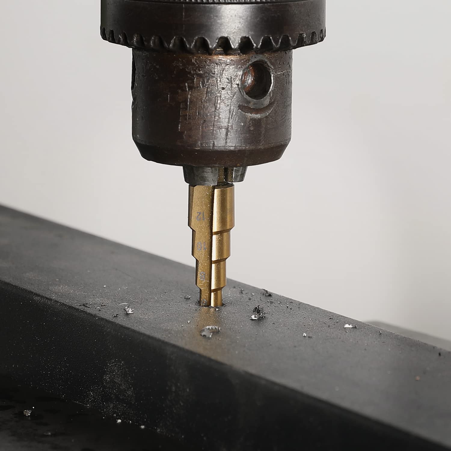 Titanium-coated step drill bit drilling into metal with stepped fluted profile