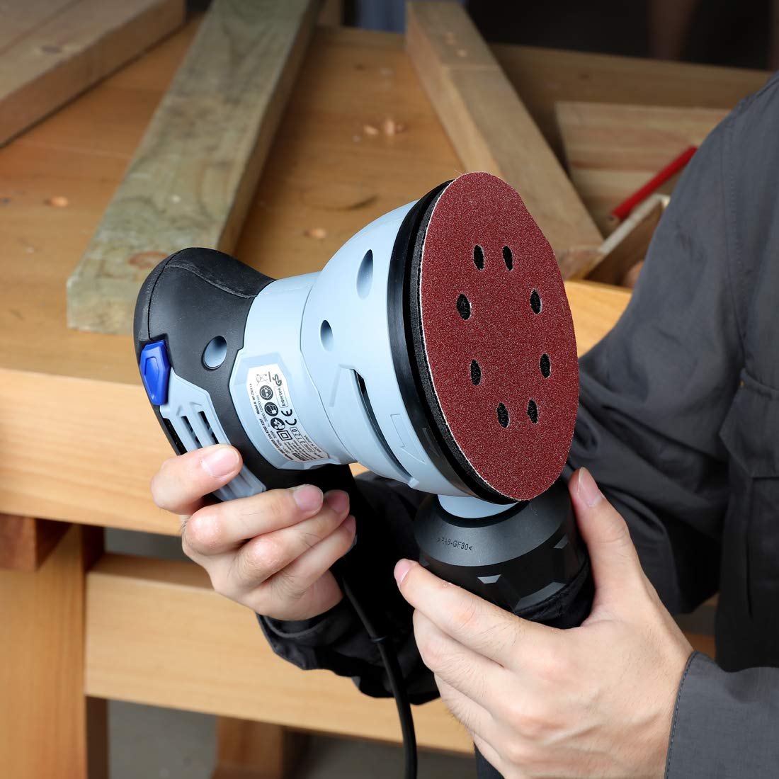 Red abrasive sanding pad with multiple holes on a random orbital sander