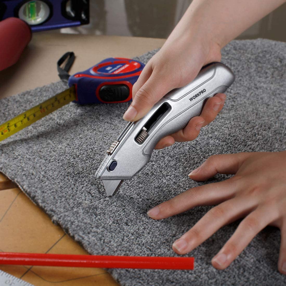 Retractable utility knife cutting along a carpet edge with hands holding the tool