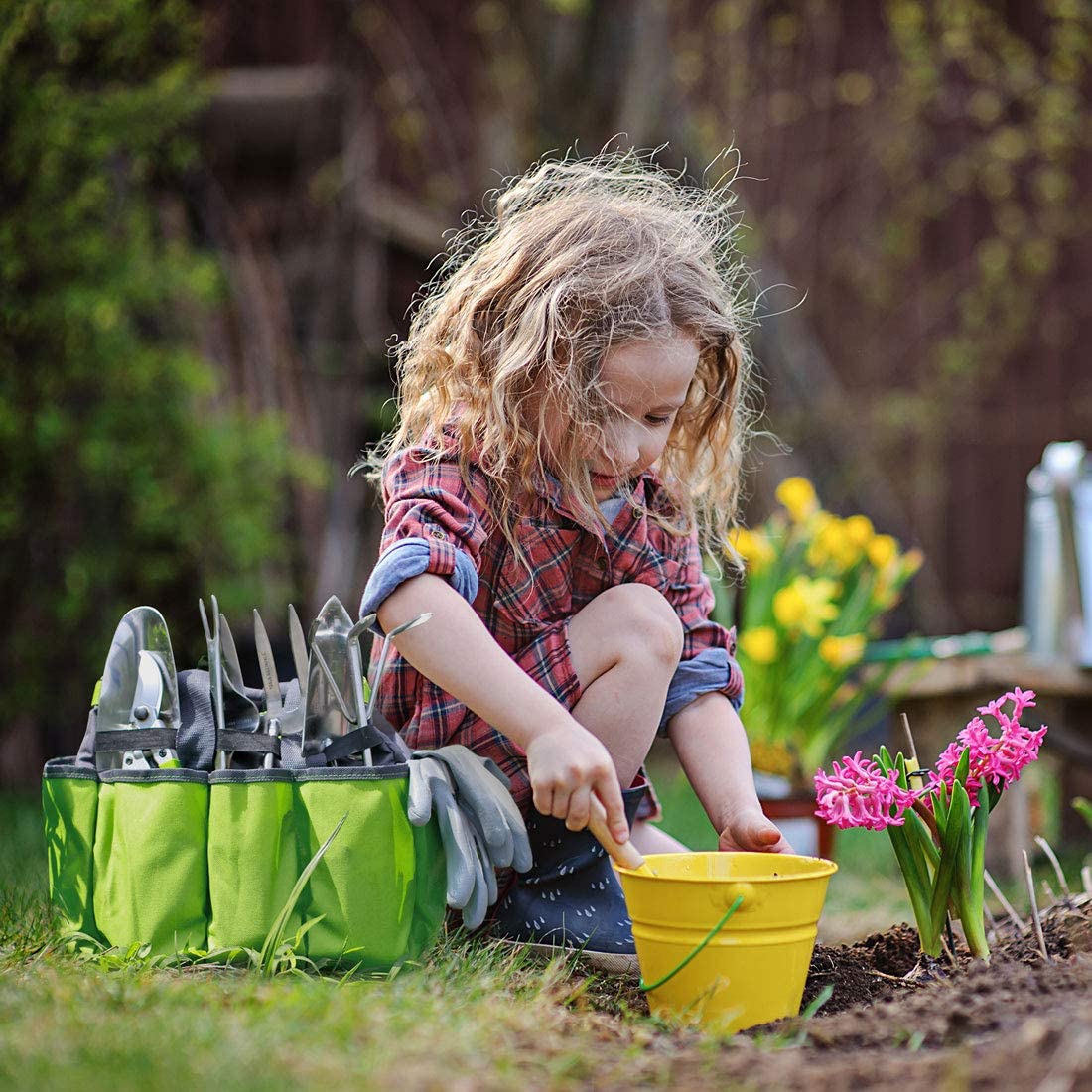 Green garden tool tote bag beside a child planting flowers in the yard