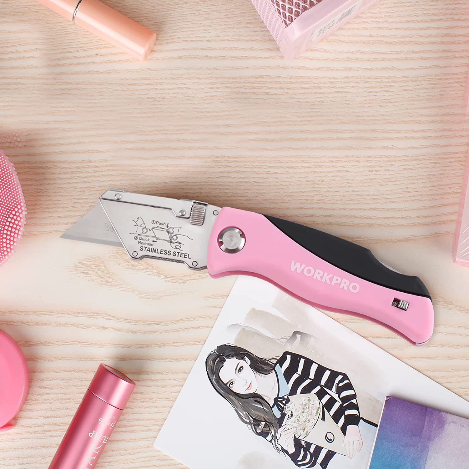 Pink WORKPRO folding utility knife with extended blade, on a wooden tabletop