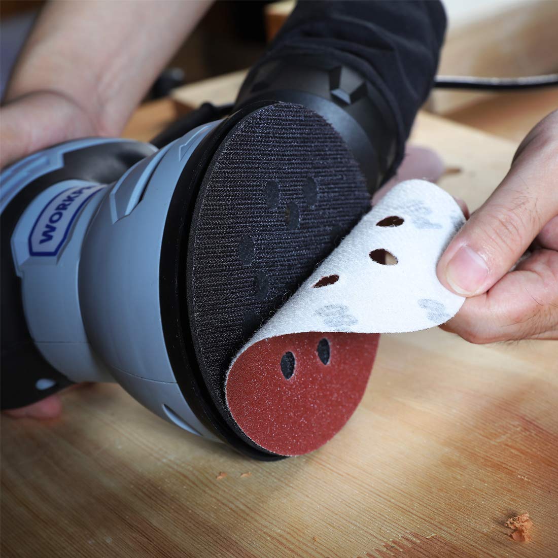 Red and white sanding disc on orbital sander, with multiple ventilation holes