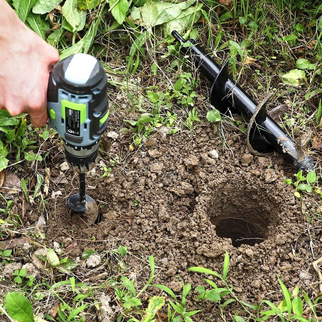 Spiral auger drill bit attached to a power drill, drilling into soil