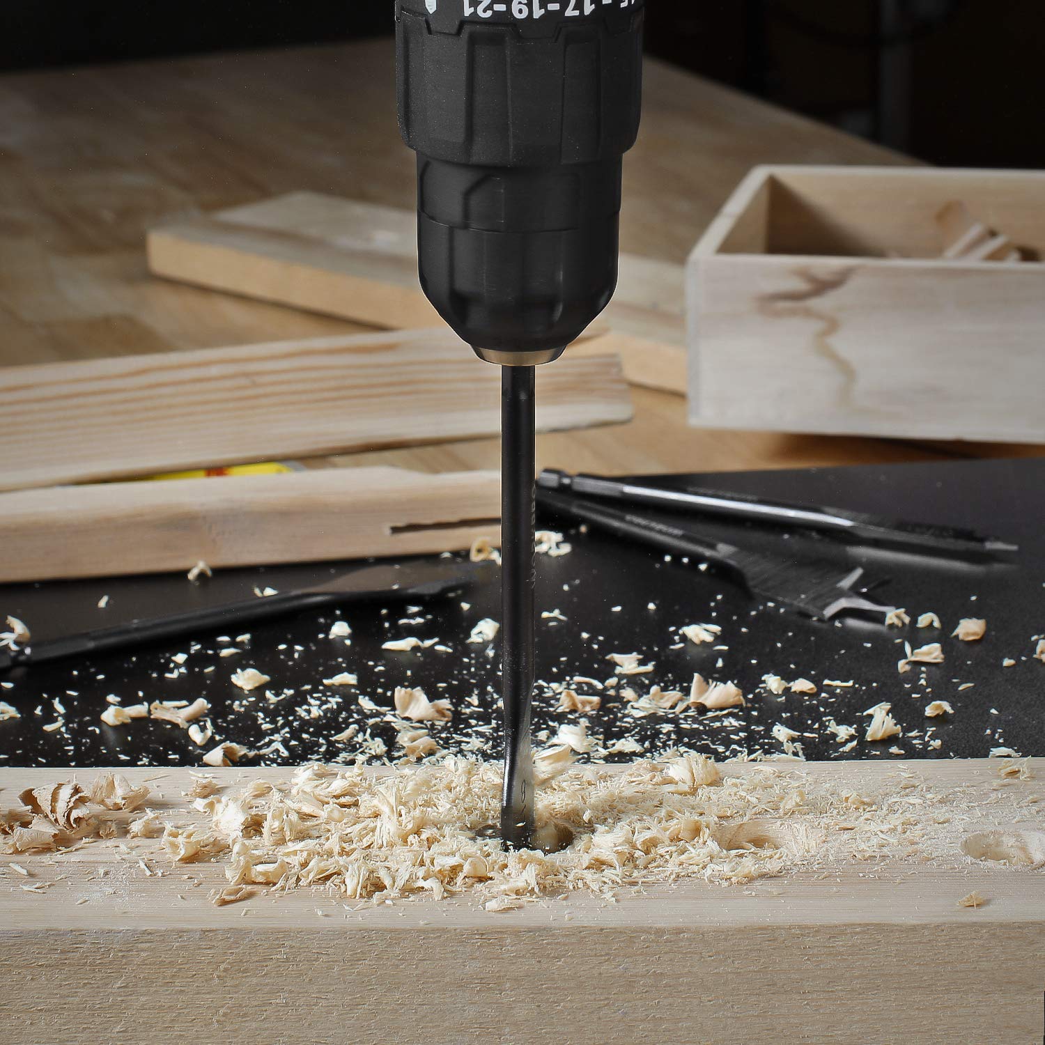 Spade drill bit drilling into a wooden board with wood shavings