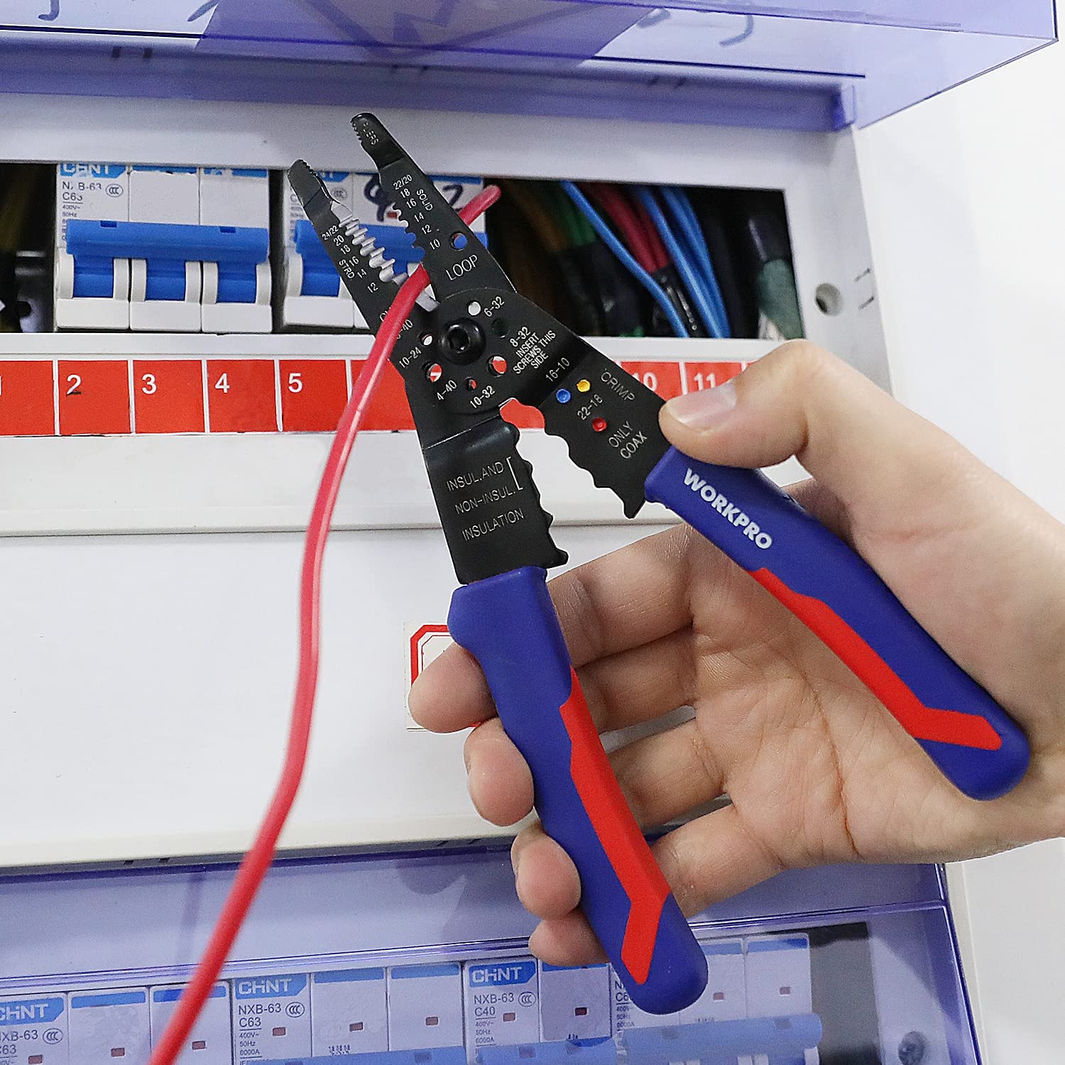 Hand holding WORKPRO wire stripping pliers gripping a red insulated wire