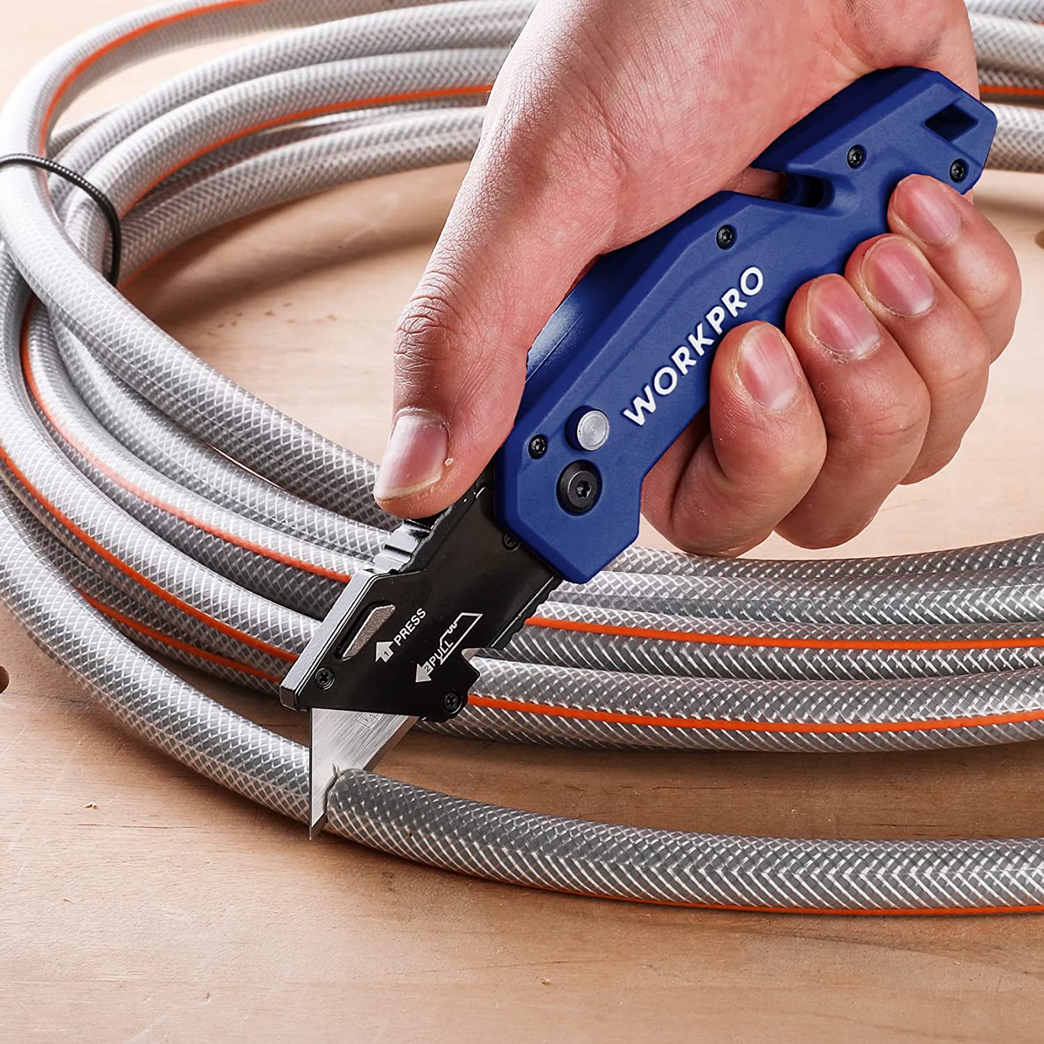 Blue folding utility knife cutting bundled cable on a work surface.