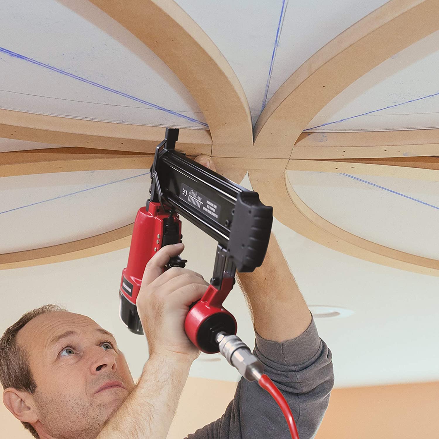 Pneumatic brad nailer held by a worker above wood framing