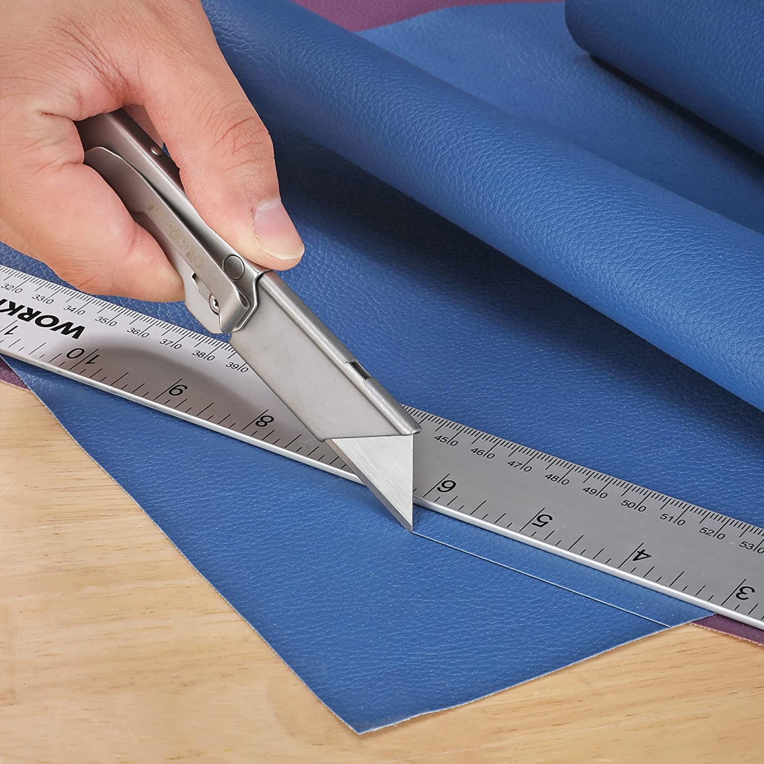 Folding utility knife cutting along a ruler on a material sheet