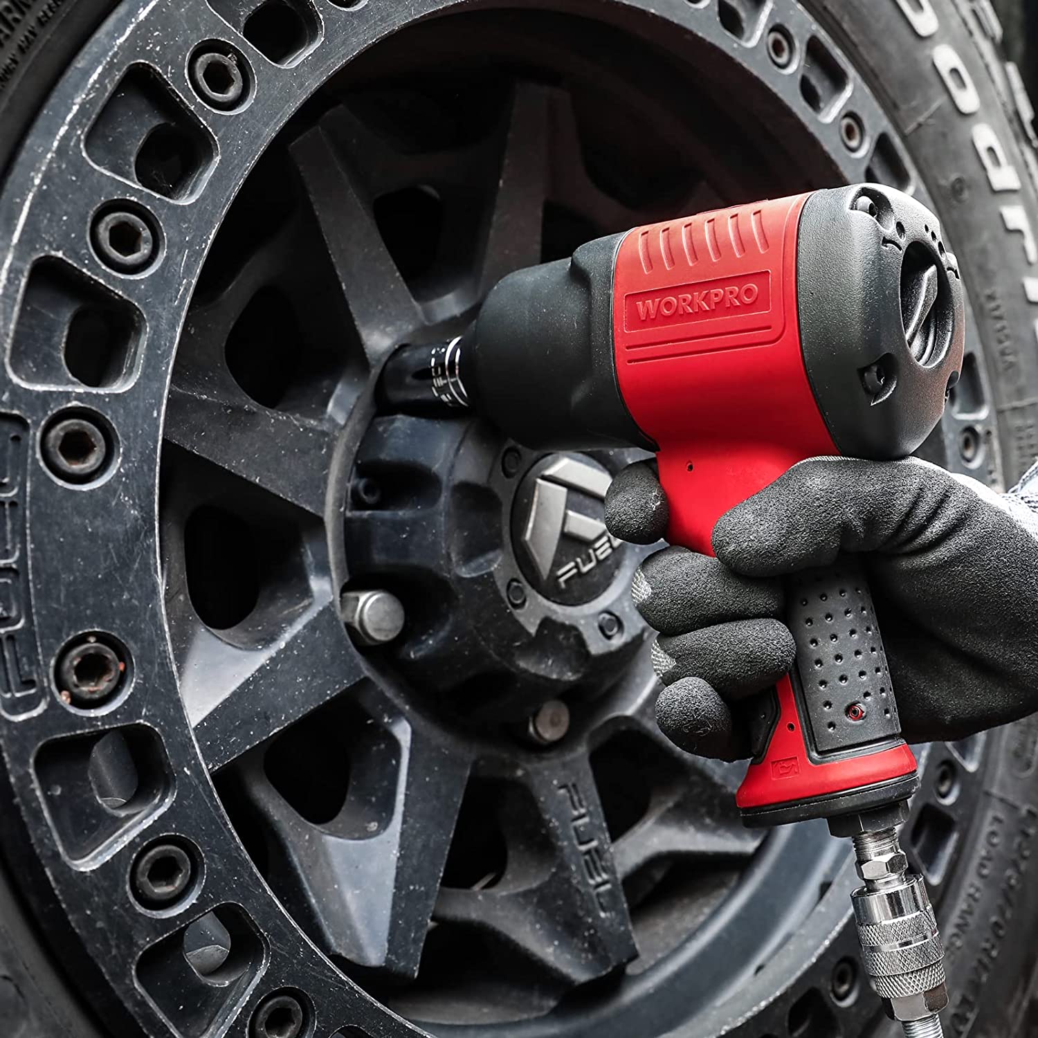 Air impact wrench in use on wheel lug area; red grip and black motor housing