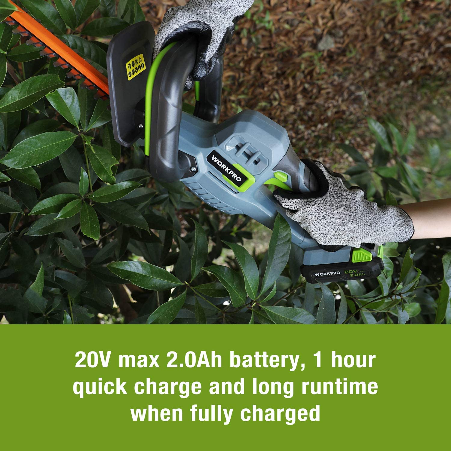 Cordless hedge trimmer in hand with orange blade and gray body, on leafy hedge