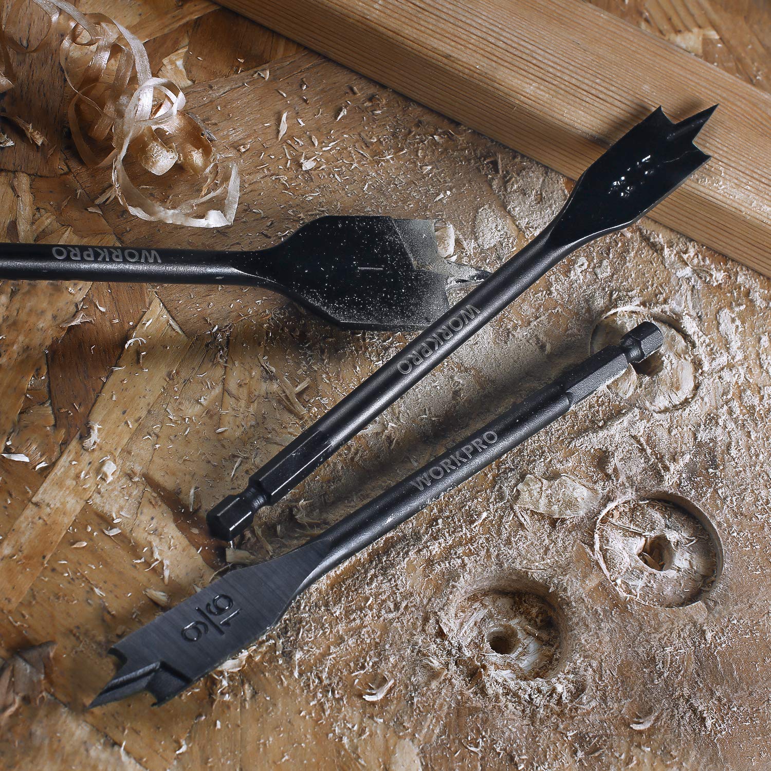 Pair of black spade drill bits on wood with drilled holes and shavings