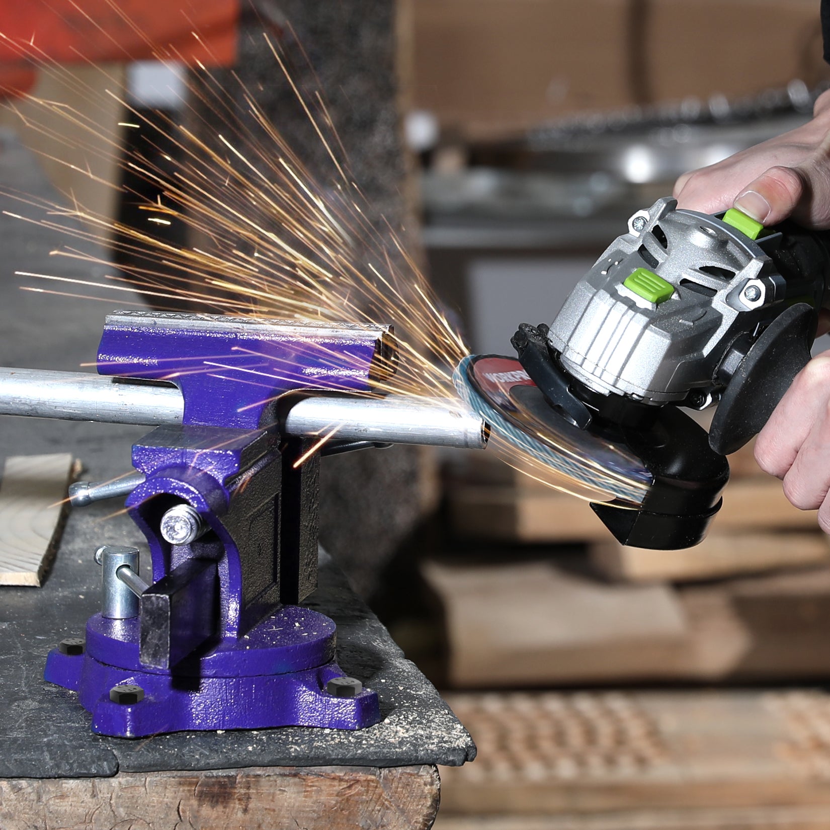 Blue bench vise on workbench with grinder cutting metal near clamped jaw