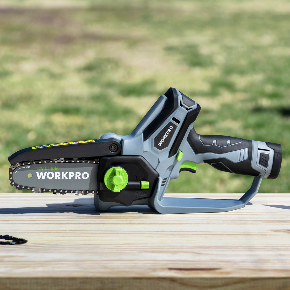 Cordless mini chainsaw resting on a wooden surface with green handle controls