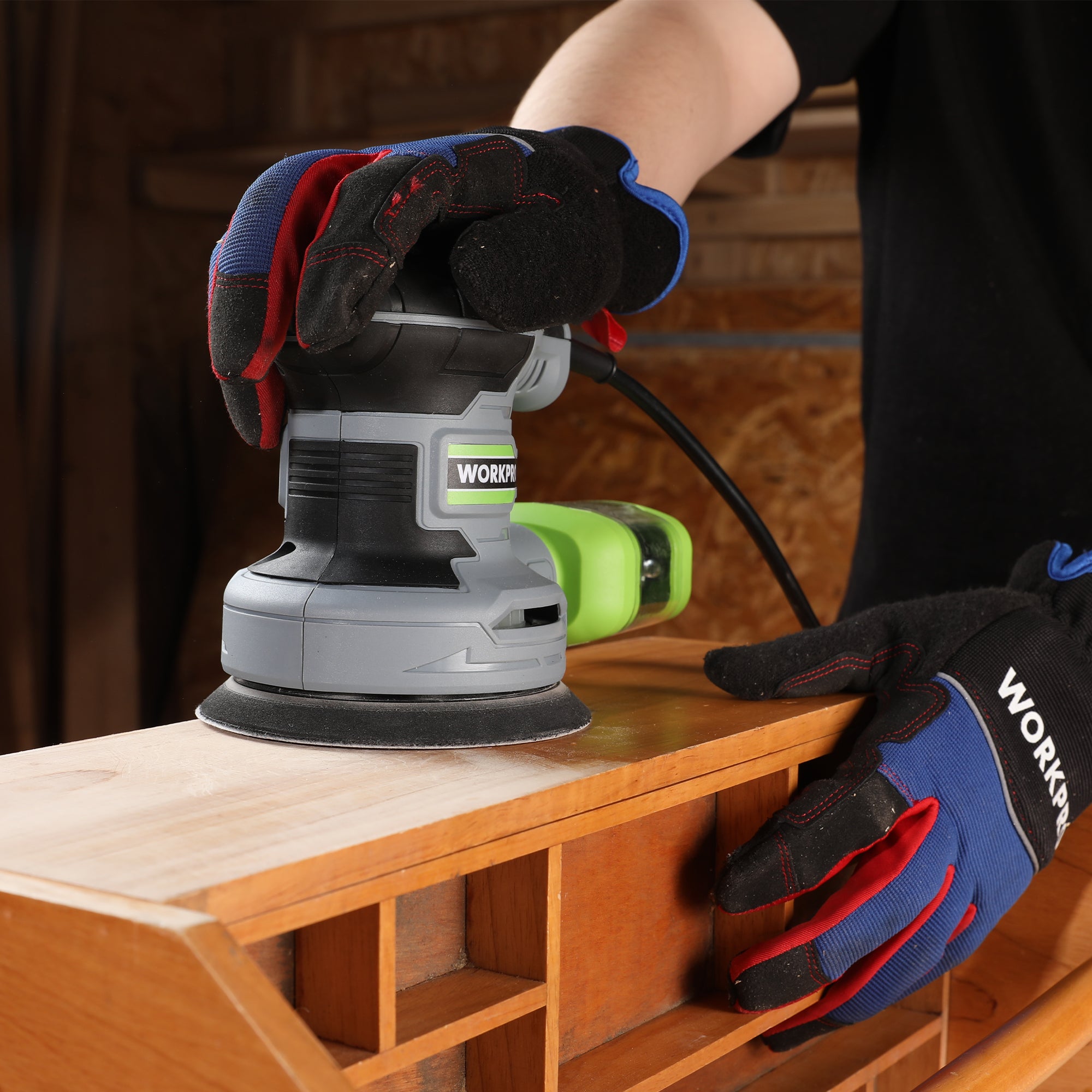 Random orbit sander in use with gloved hands on a wooden surface
