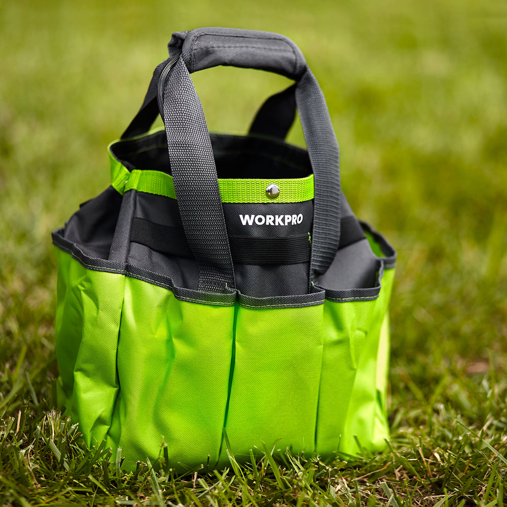 Green gardening tool tote bag standing on grass with black handles and front pockets