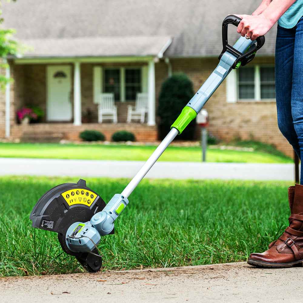 Cordless string trimmer edging near a sidewalk with operator foot and hand