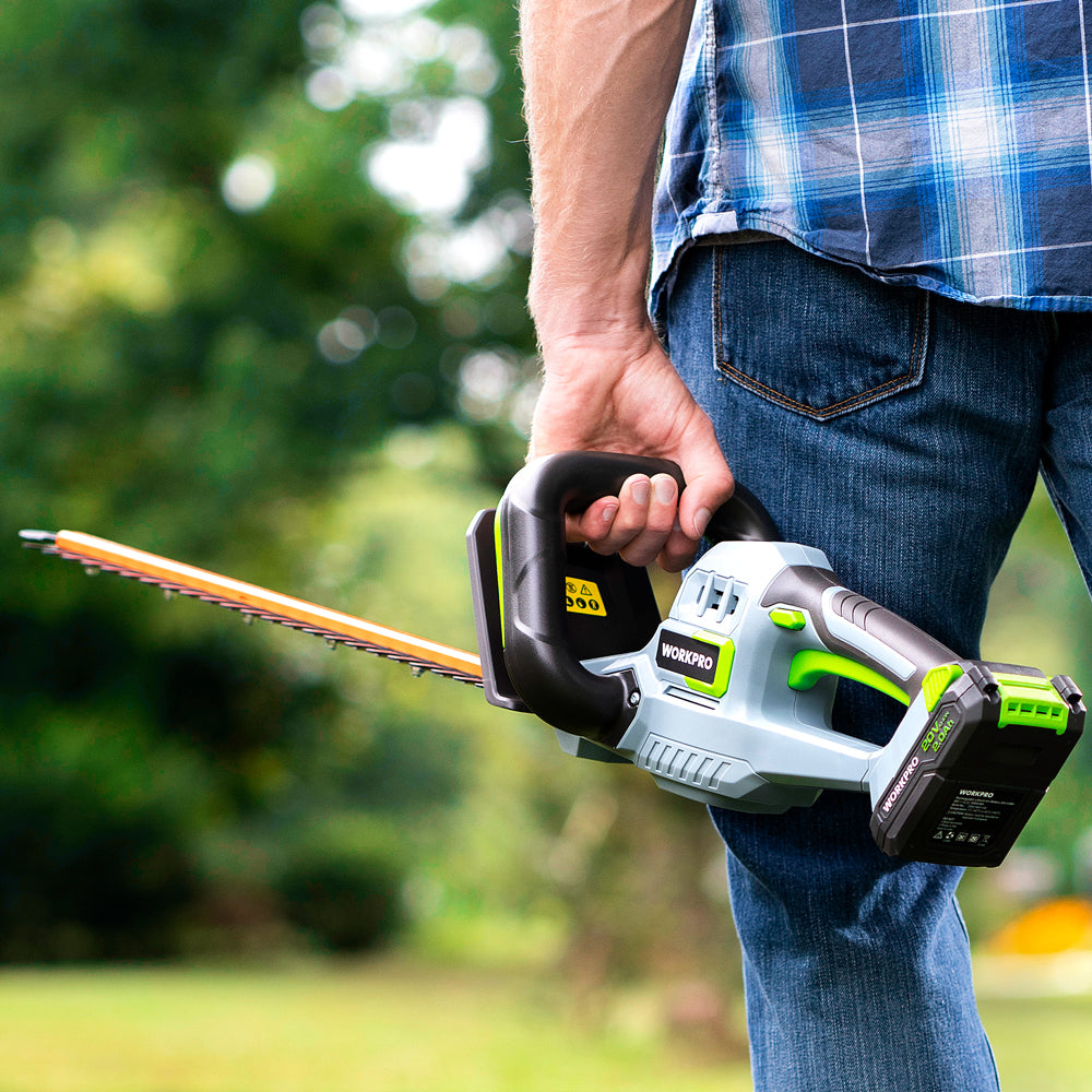 Handheld hedge trimmer with orange blade, gray body, and green battery pack