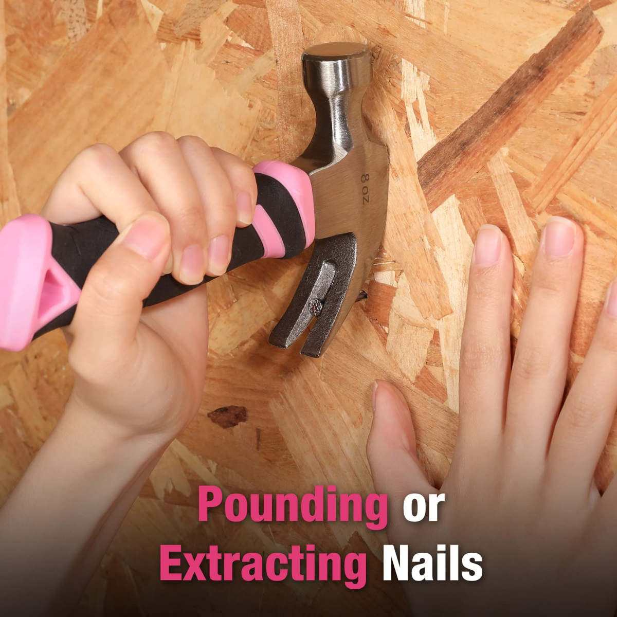 Claw hammer in hand on wood: black handle with pink grip, silver claw and head.