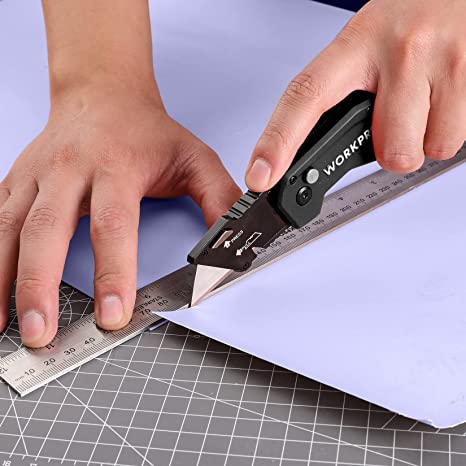 Blue folding utility knife with black blade cutting sheet material with ruler.